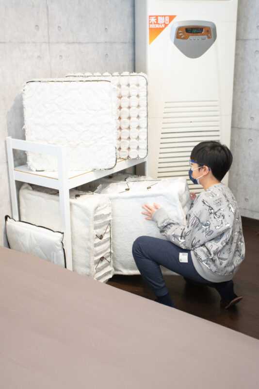 男性蹲在床墊剖面展示品旁查看內部結構