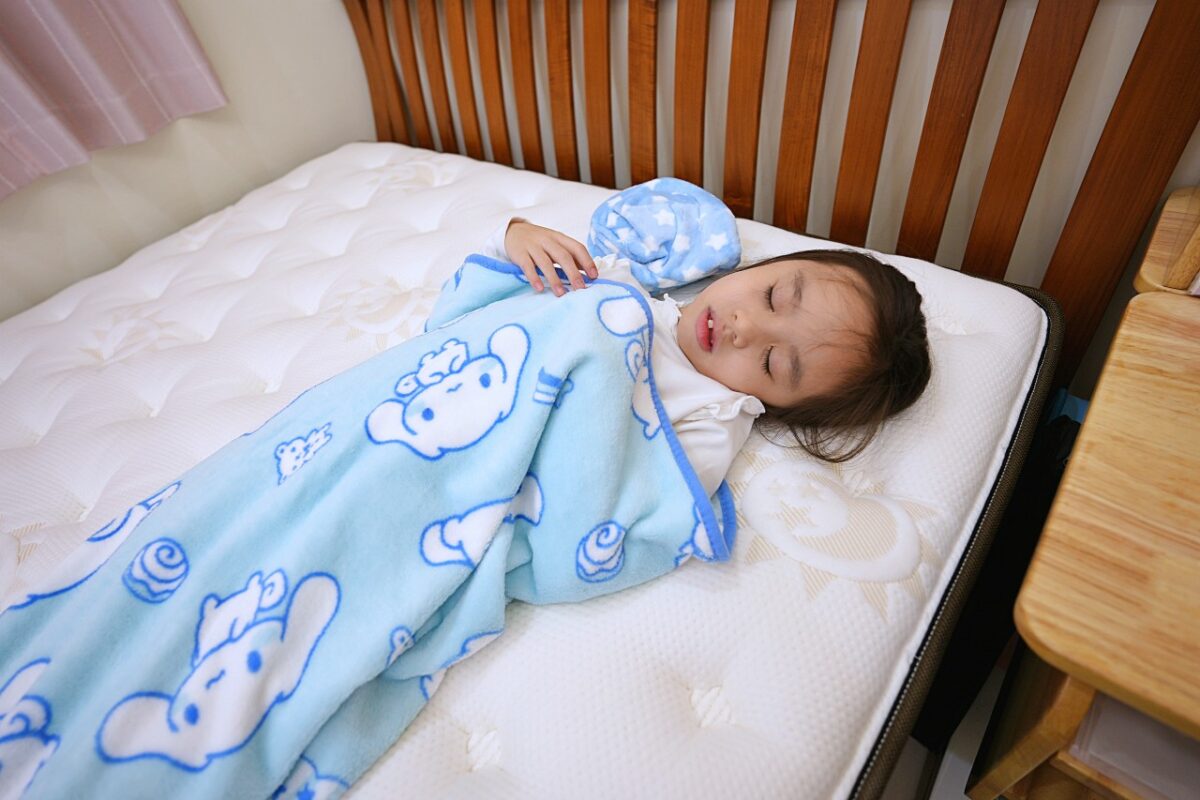 小女孩蓋著毯子睡在曙光床墊上